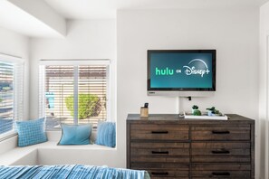 Une chambre à coucher avec un grand téléviseur à écran plat fixé au mur, sur lequel apparaît le logo de Hulu.