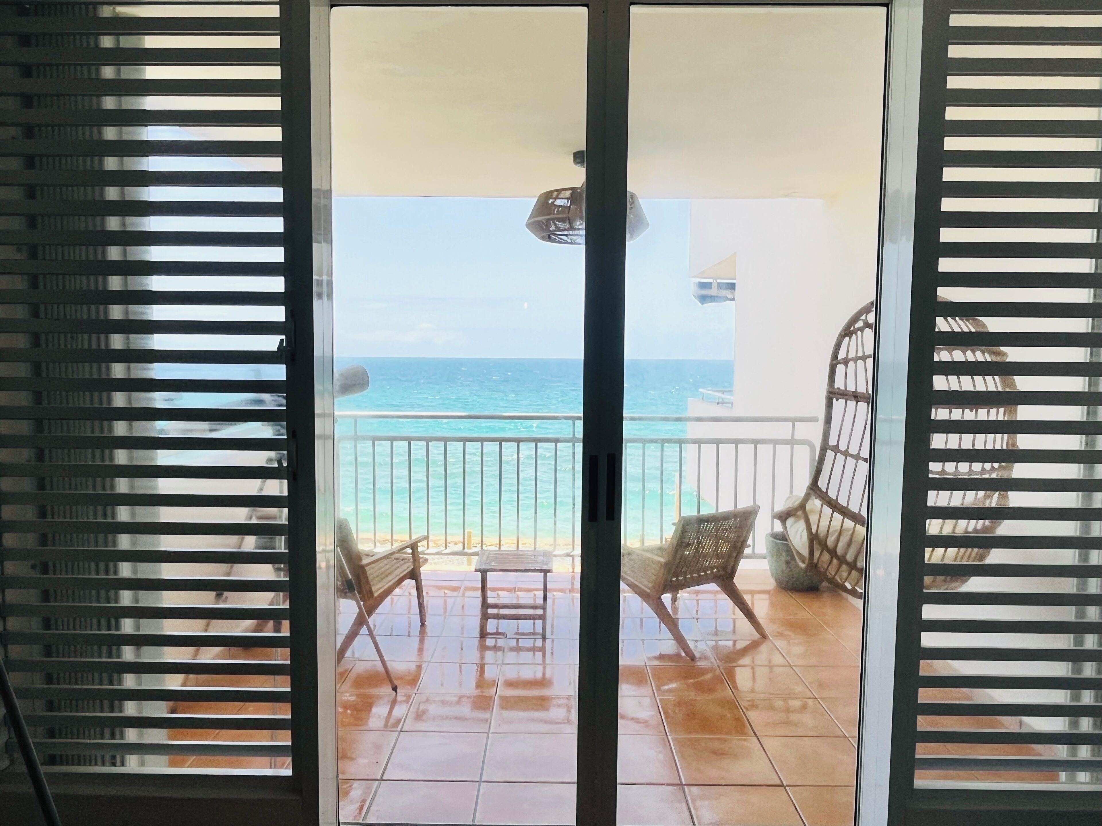 Un balcon avec deux fauteuils en osier et une petite table, d’où l’on peut admirer une plage et l’océan.