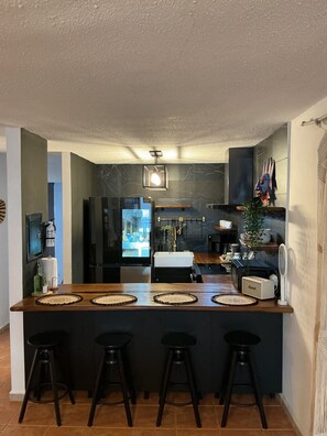 A modern kitchen with a central island, bar stools, a refrigerator, and a microwave.