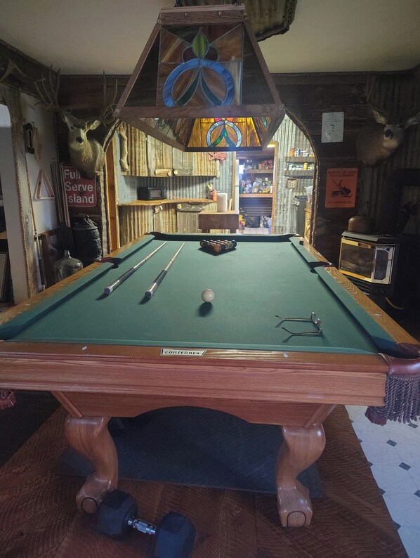 A pool table with a wooden frame, a cue stick, and a pool ball.
