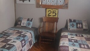 Quarto com duas camas, uma cadeira de madeira, um número '25' fixado na parede e um quadro com passarinhos.