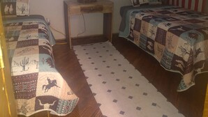 Quarto com duas camas, uma mesa de cabeceira, um abajur, uma janela e uma bandeira americana na parede.