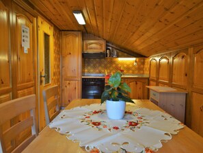 Een houten interieur met een eettafel, stoelen, een fornuis en kastjes.