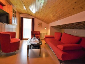 Ein gemütliches Zimmer mit Holzbalkendecke, einem roten Sofa, einem roten Sessel und einem Glastisch.