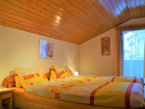 A bedroom with a wooden ceiling, two beds with colorful quilts, a bedside table, and a window with curtains. - Glacier-Sport, (Grächen), 1053 by Interhome (Grächen)