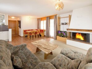 Ein Wohnzimmer mit Kamin, einer Sofagarnitur, einem Essbereich mit Tisch und Stühlen sowie einer Küche.