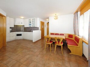 Eine kleine Küche mit weißen Schränken und einem Essbereich mit einem Holztisch und roten Stühlen.