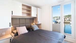 Et soveværelse med seng, indbygget opbevaring, et vindue med udsigt til både og et natbord med lampe.