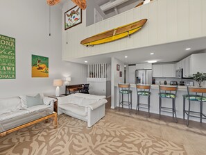 A modern kitchen with white cabinets, a stainless steel refrigerator, and a bar area with stools. - Sunset, Ocean, and Golf Course Views! (Waikoloa Village)