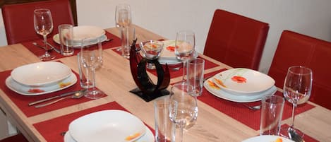A dining table set with plates, glasses, and cutlery, surrounded by red chairs.