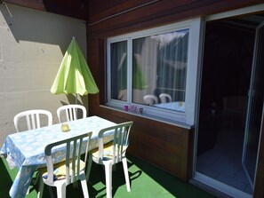 A patio with a table and chairs, a green umbrella, and a window with a view of mountains. - Brunegghorn Biner, (Grächen), 1104 by Interhome (Grächen)