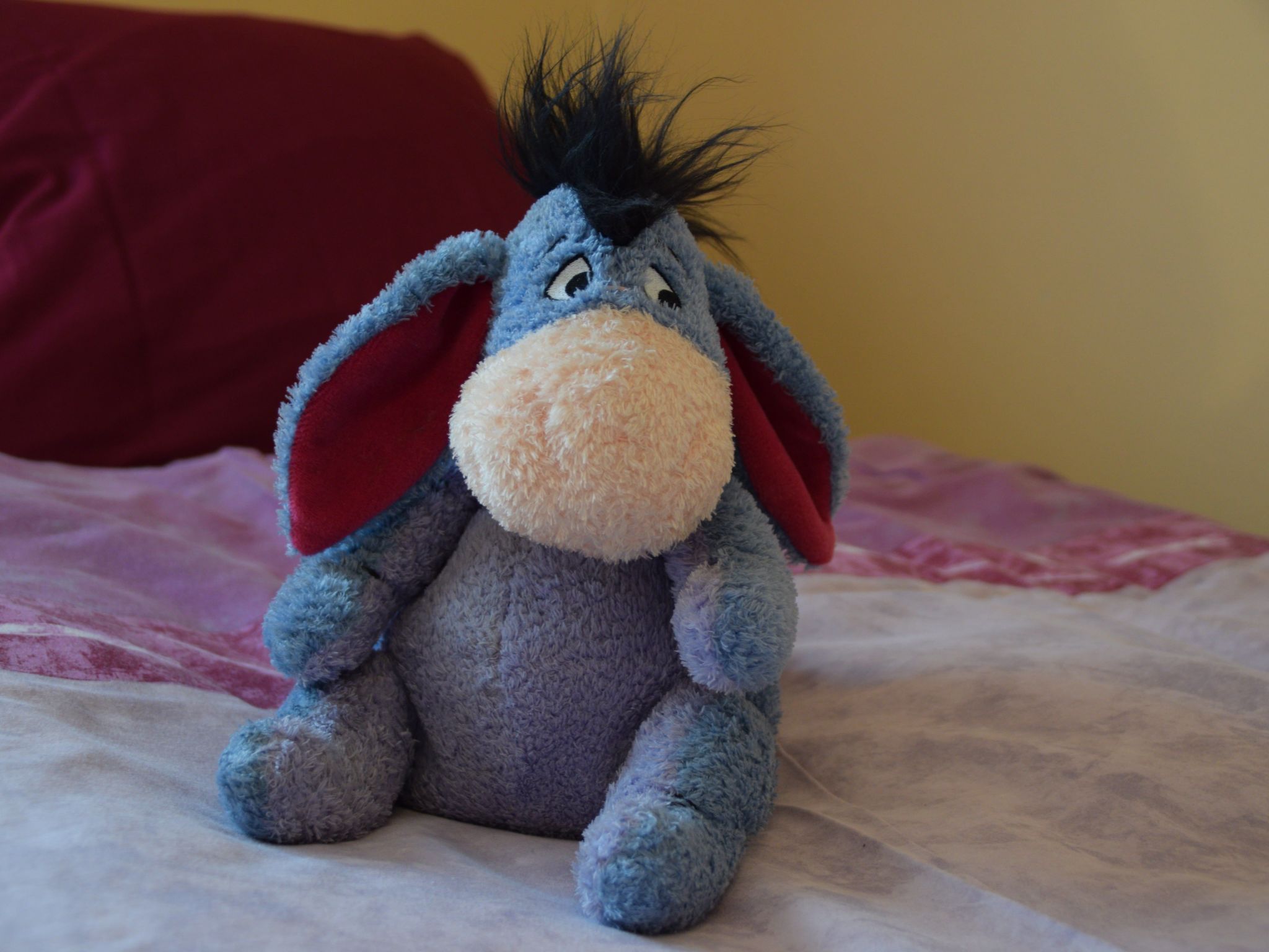 Un peluche su un letto con un cuscino rosso.