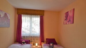 Quarto com duas camas, janela com cortinas, mesa de cabeceira com abajur e obras de arte nas paredes.
