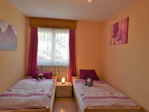A bedroom with two beds, a window with curtains, a nightstand with a lamp, and artwork on the walls. - Brunegghorn Biner, (Grächen), 1104 by Interhome (Grächen)