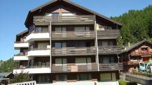 Um edifício com várias andares e varandas, possivelmente um hotel ou complexo de apartamentos, cercado por vegetação.