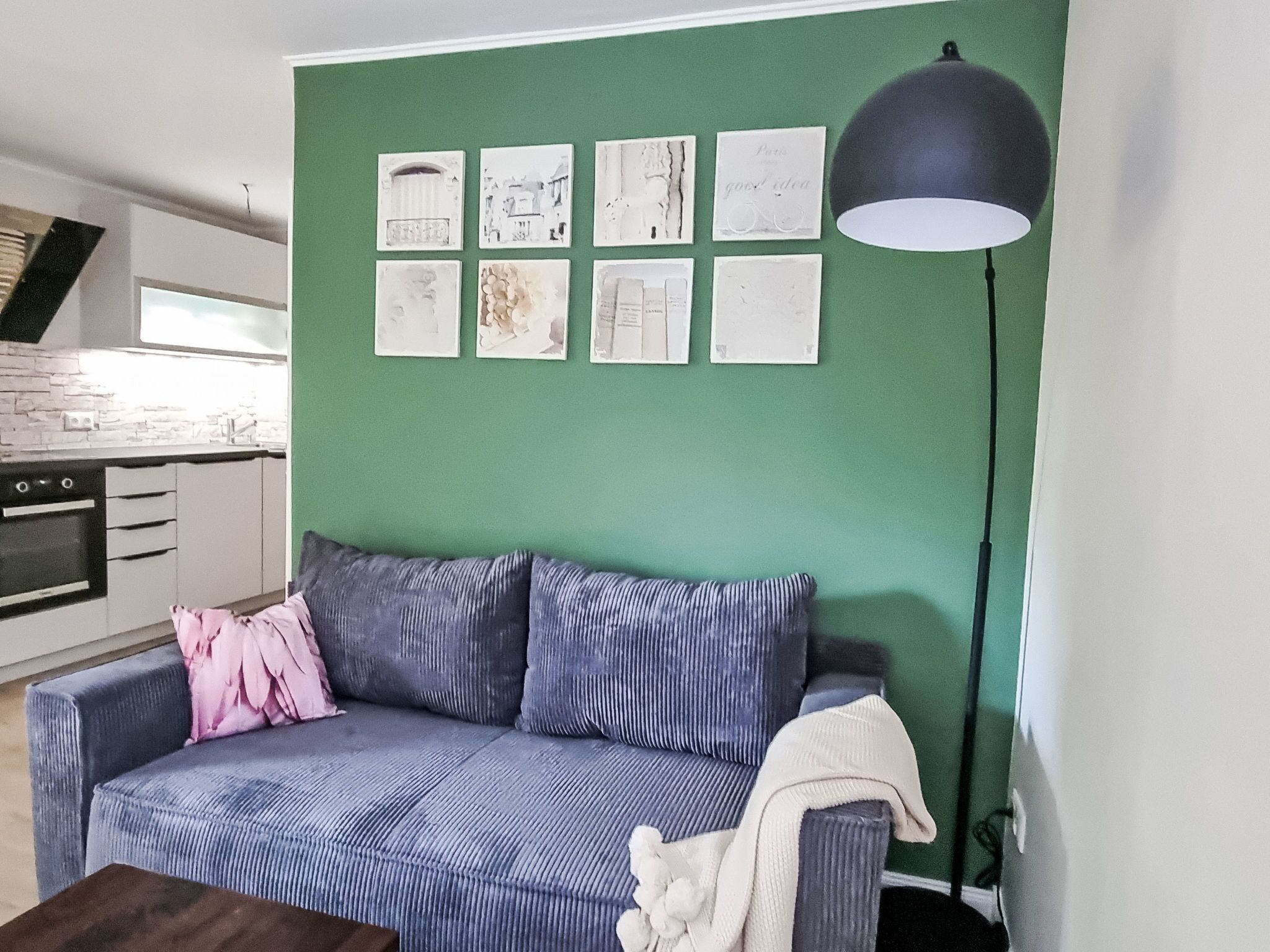 Ein Wohnzimmer mit grüner Wand, einer Couch, einem Couchtisch und einer Stehlampe.