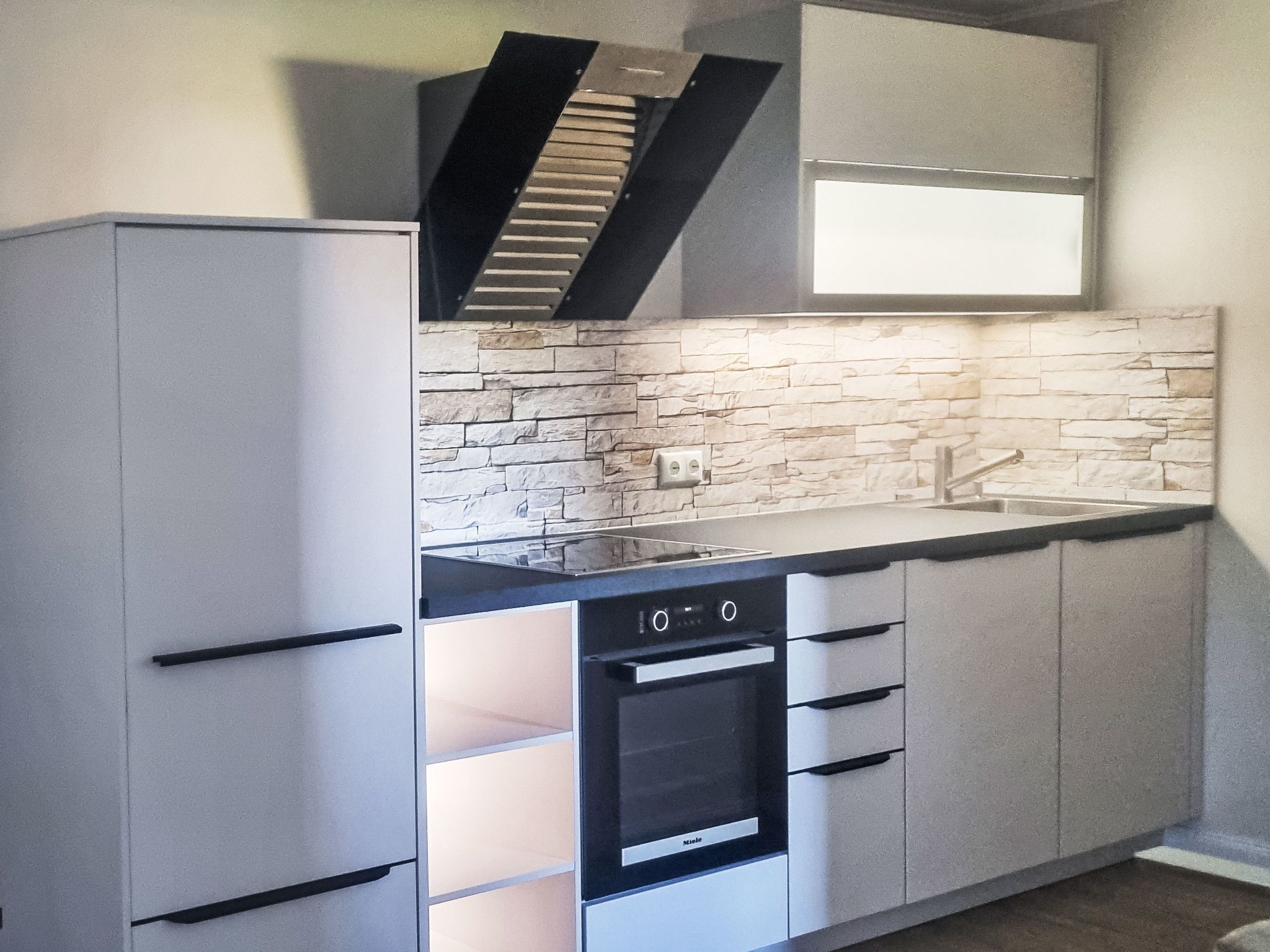 A kitchen with a built-in oven, a stovetop, and a backsplash made of stone tiles.