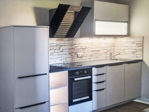 A kitchen with a built-in oven, a stovetop, and a backsplash made of stone tiles. - Gästehaus am Neetzekanal by Interhome (Bardowick)