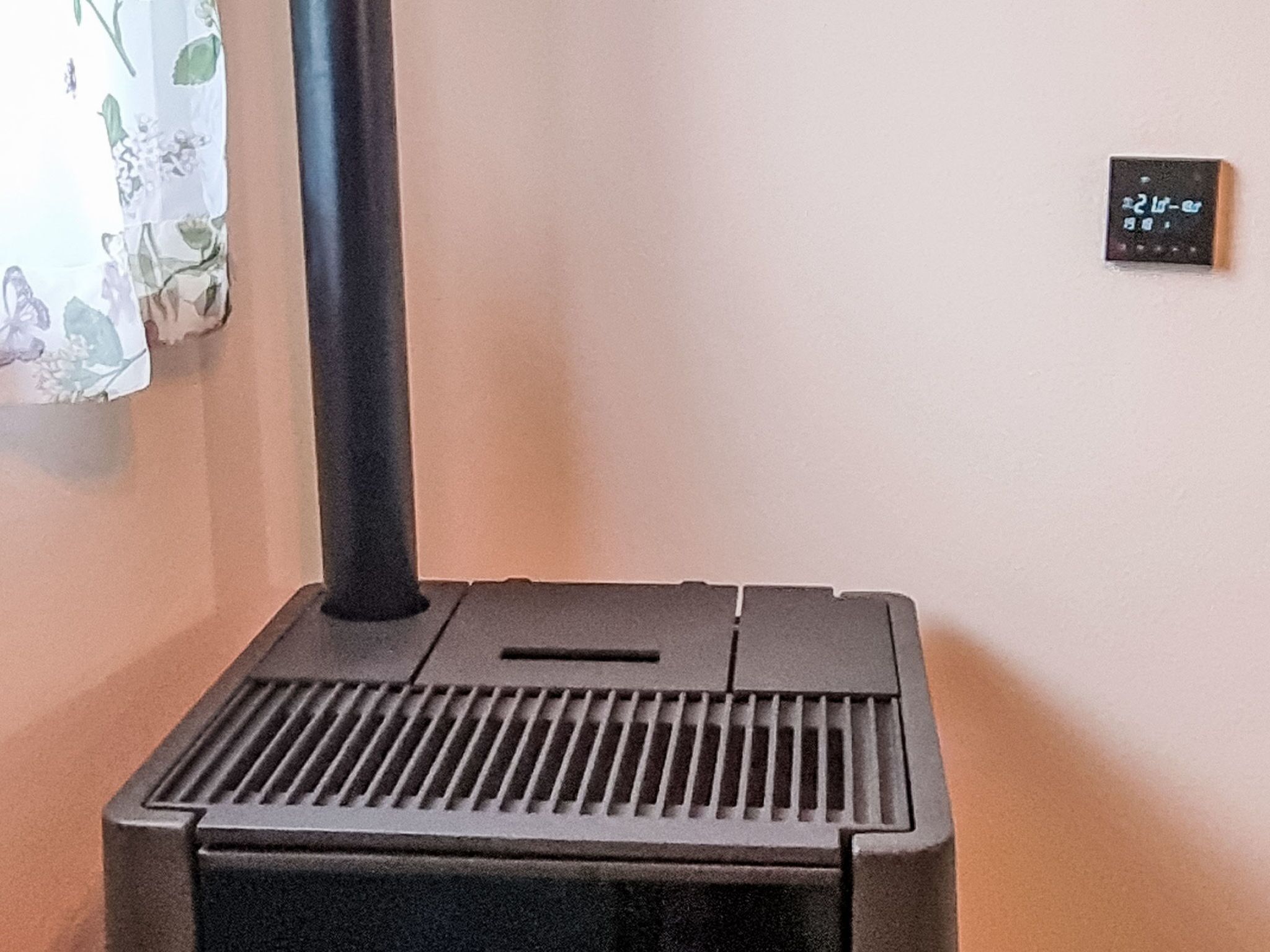 Een zwarte, draagbare heater met ventilatieopening en bedieningspaneel, geplaatst tegen een muur met een stopcontact en een schakelaar.