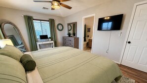 A bedroom with a bed, a television, a ceiling fan, a desk, and a bathroom visible through an open door. - Route 66 River House: 8 Min to Boat Launch, Boat & Trailer Parking (Mohave Valley)