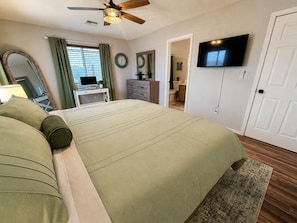 A bedroom with a bed, a television, a ceiling fan, a desk, and a bathroom visible through an open door. - Route 66 River House: 8 Min to Boat Launch, Boat & Trailer Parking (Mohave Valley)