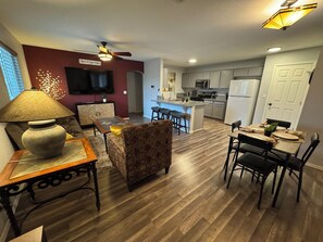 A modern living room with a sofa, a coffee table, and a TV. There is a kitchen area with a refrigerator, microwave, and bar stools. - Route 66 River House: 8 Min to Boat Launch, Boat & Trailer Parking (Mohave Valley)
