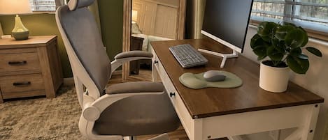 A room with a desk, chair, computer, and a potted plant.