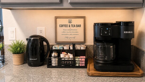A kitchen counter with a Keurig coffee maker, a coffee station with cups and a sign, and a potted plant. - Route 66 River House: 8 Min to Boat Launch, Boat & Trailer Parking (Mohave Valley)
