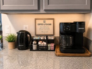 Un comptoir de cuisine avec une machine à café Keurig, un espace dédié au café avec des tasses et un panneau, et une plante en pot.