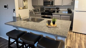 A modern kitchen with granite countertops, stainless steel appliances, and a central island with bar stools. - Route 66 River House: 8 Min to Boat Launch, Boat & Trailer Parking (Mohave Valley)