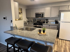 A modern kitchen with granite countertops, stainless steel appliances, and a central island with bar stools. - Route 66 River House: 8 Min to Boat Launch, Boat & Trailer Parking (Mohave Valley)