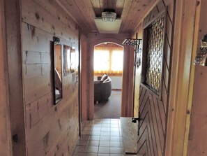 En hall med träpanel och ett klinkergolv som leder till ett rum med en bekväm sittgrupp och ett fönster med gardiner.