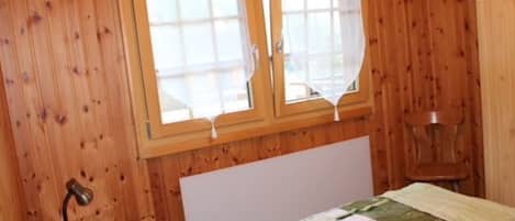 Ein Zimmer mit Holzwänden, einem Bett, einer Nachttischlampe und einem fenster mit Vorhängen.
