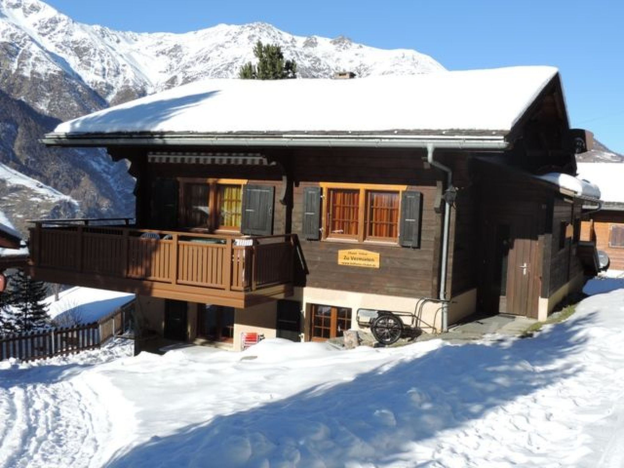 Un chalet en bois doté d’un balcon, situé au pied d’une montagne enneigée.