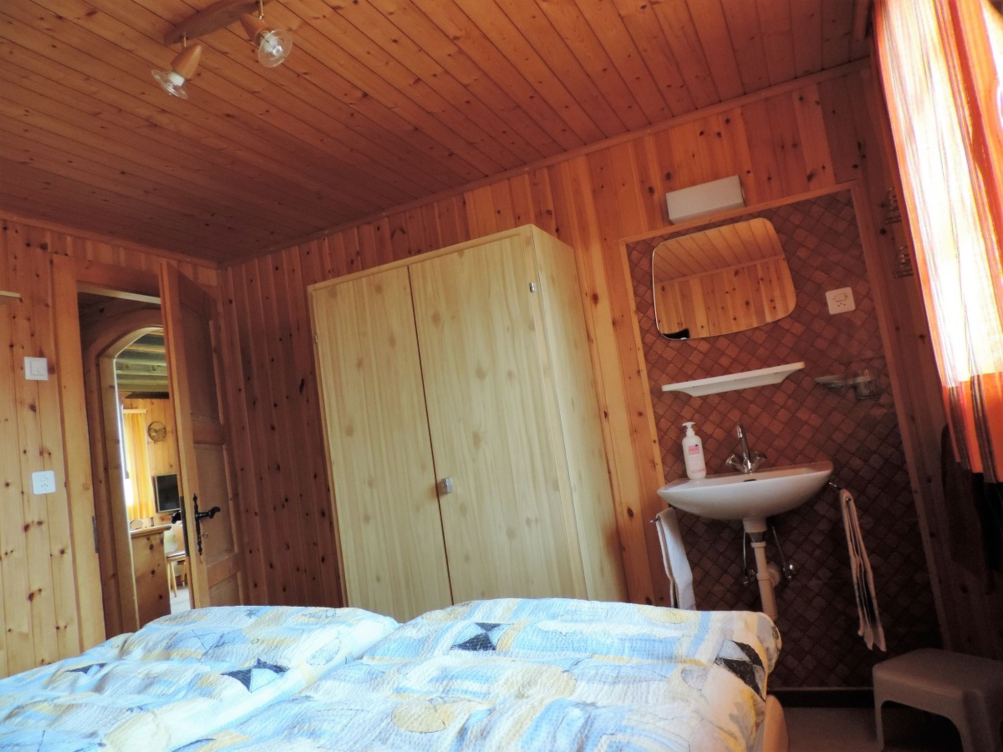 A wooden room with a bed, a wardrobe, a mirror, and a sink.