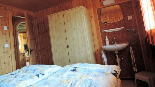 A wooden room with a bed, a wardrobe, a mirror, and a sink. - Föhre, (Grächen), 1420 by Interhome (Grächen)