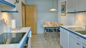 Kompakti keittiö, jossa on sisäänrakennettu liesi, ruokailutila pöydän ja tuolien kera sekä puinen ovi.