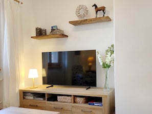A flat-screen TV on a wooden stand with a lamp and a vase of flowers.