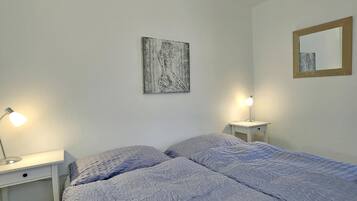 A bedroom with a bed, two bedside tables, a lamp, a painting, and a mirror.