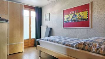 A bedroom with a bed, a wardrobe, a radiator, a window with curtains, and a wall with a colorful poster.
