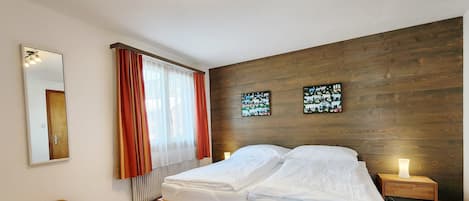 A bedroom with a wooden bed, a nightstand with a lamp, a radiator, and two wall art pieces.