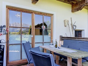 Ein Essbereich mit Tisch und Stühlen, Blick auf Berge durch große Fenster und eine rustikale Holzzieldecke.