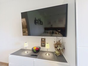 Ein Flachbildfernseher ist an einer Wand über einer weißen Ablage mit zwei Lampen und einer Dekoschale befestigt.