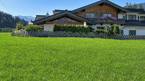 Un chalet à deux étages, doté d’un toit en pente, d’une façade en bois et d’un balcon orné de fleurs violettes.