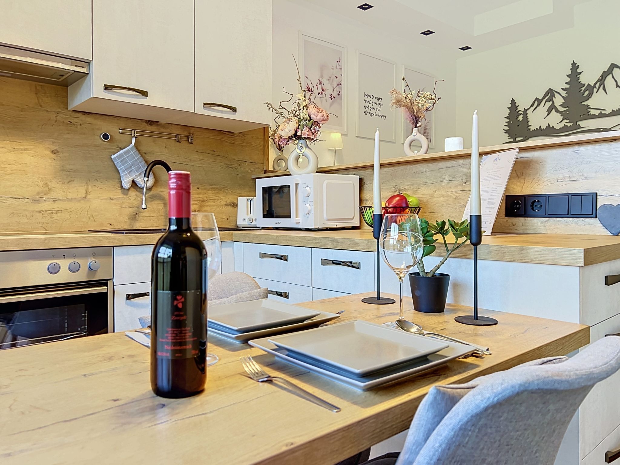 A modern kitchen with a wooden countertop, a wine bottle, a microwave, and a dining area with a table set for two.