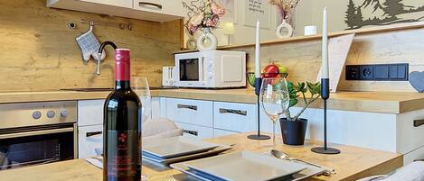 A modern kitchen with a wooden countertop, a wine bottle, a microwave, and a dining area with a table set for two.