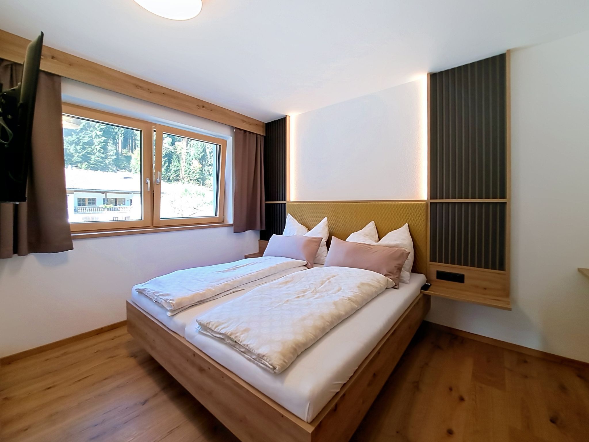 Een slaapkamer met een houten bed, een raam met gordijnen en een wandlamp.