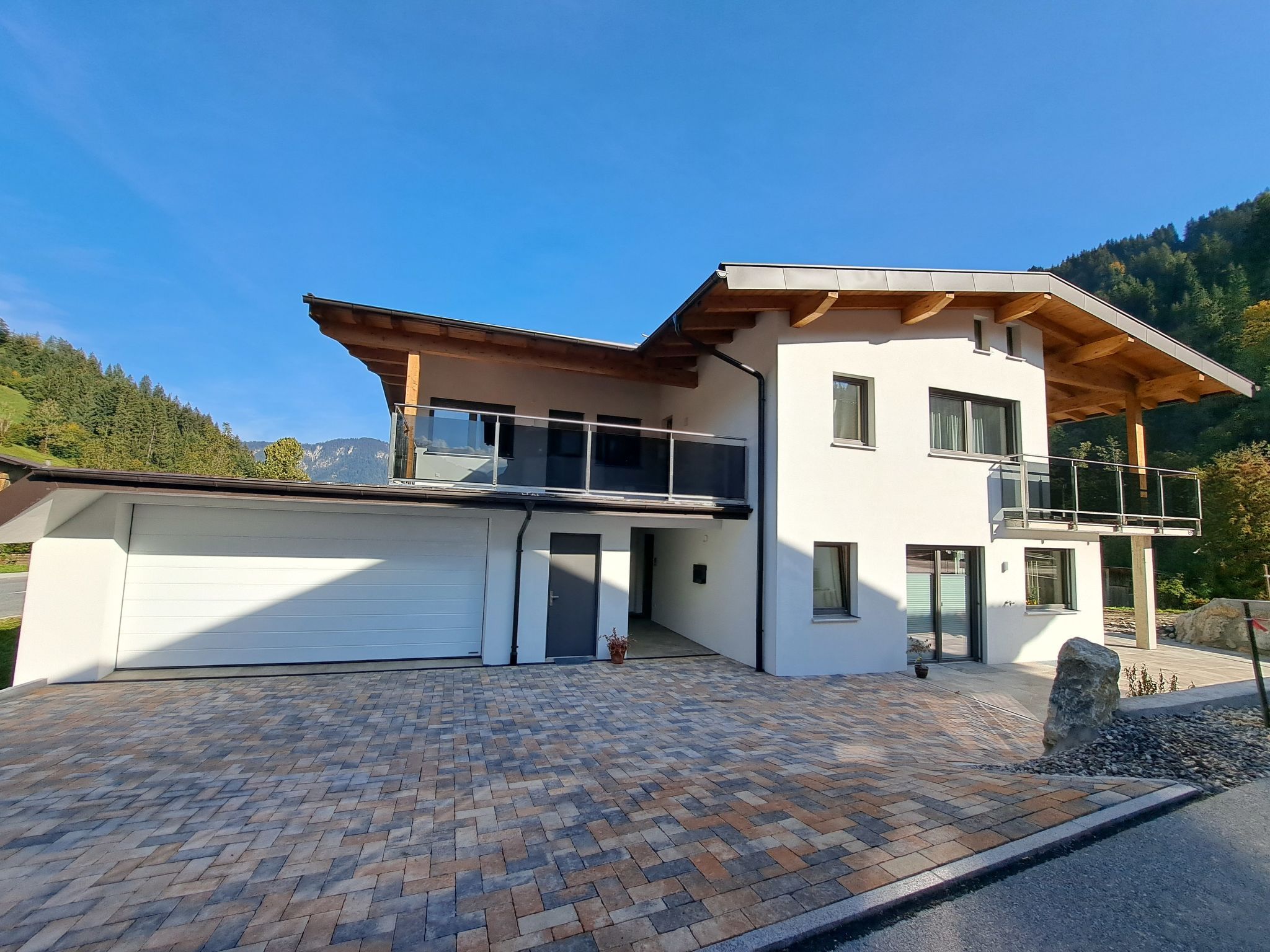 Een modern huis met twee verdiepingen, een garage, een balkon en uitzicht op de bergen.