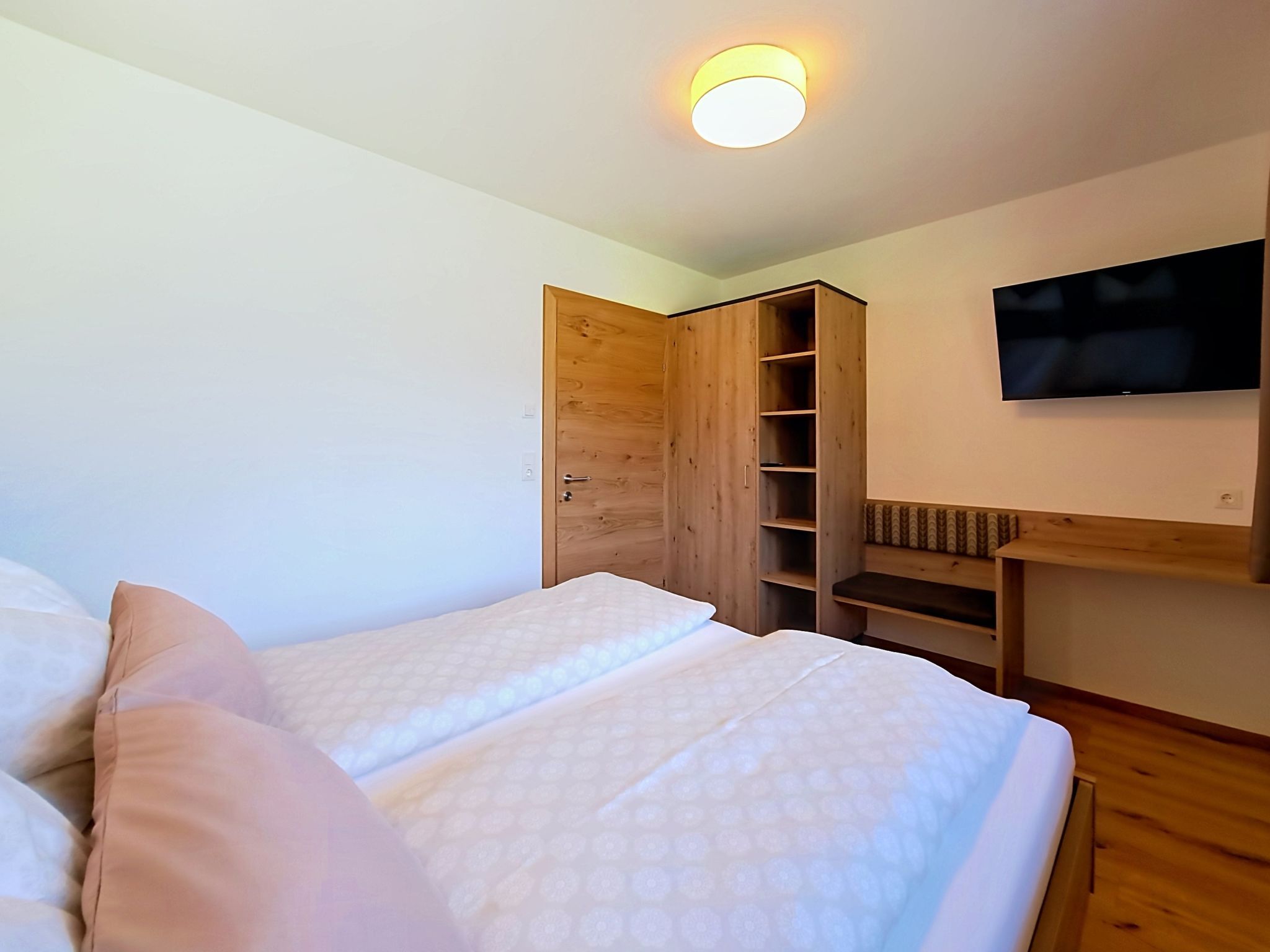 Une chambre avec deux lits, une armoire en bois, une télévision et un luminaire au plafond.