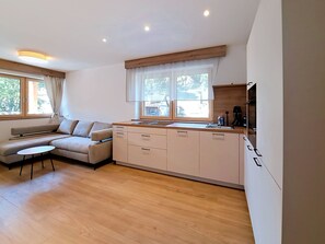 A modern kitchen with a built-in oven, a dining area with a sofa, and a large window providing natural light. - Apartment Tyrol by Interhome (Auffach)